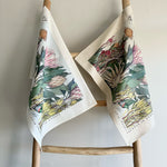 Load image into Gallery viewer, Two fynbos and protea floral-patterned towels hanging on a wooden rack against a plain background