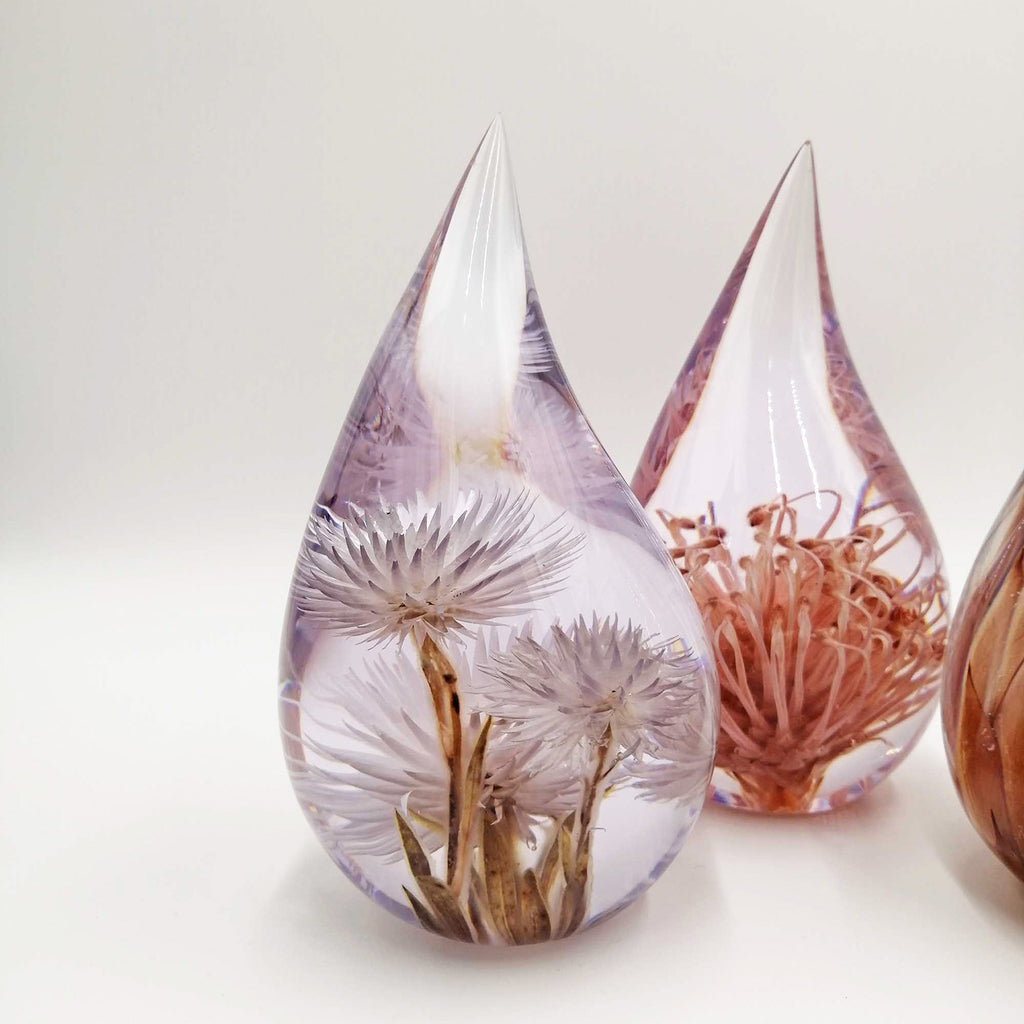 Teardrop-shaped resin pieces with preserved fynbos and protea on a white background