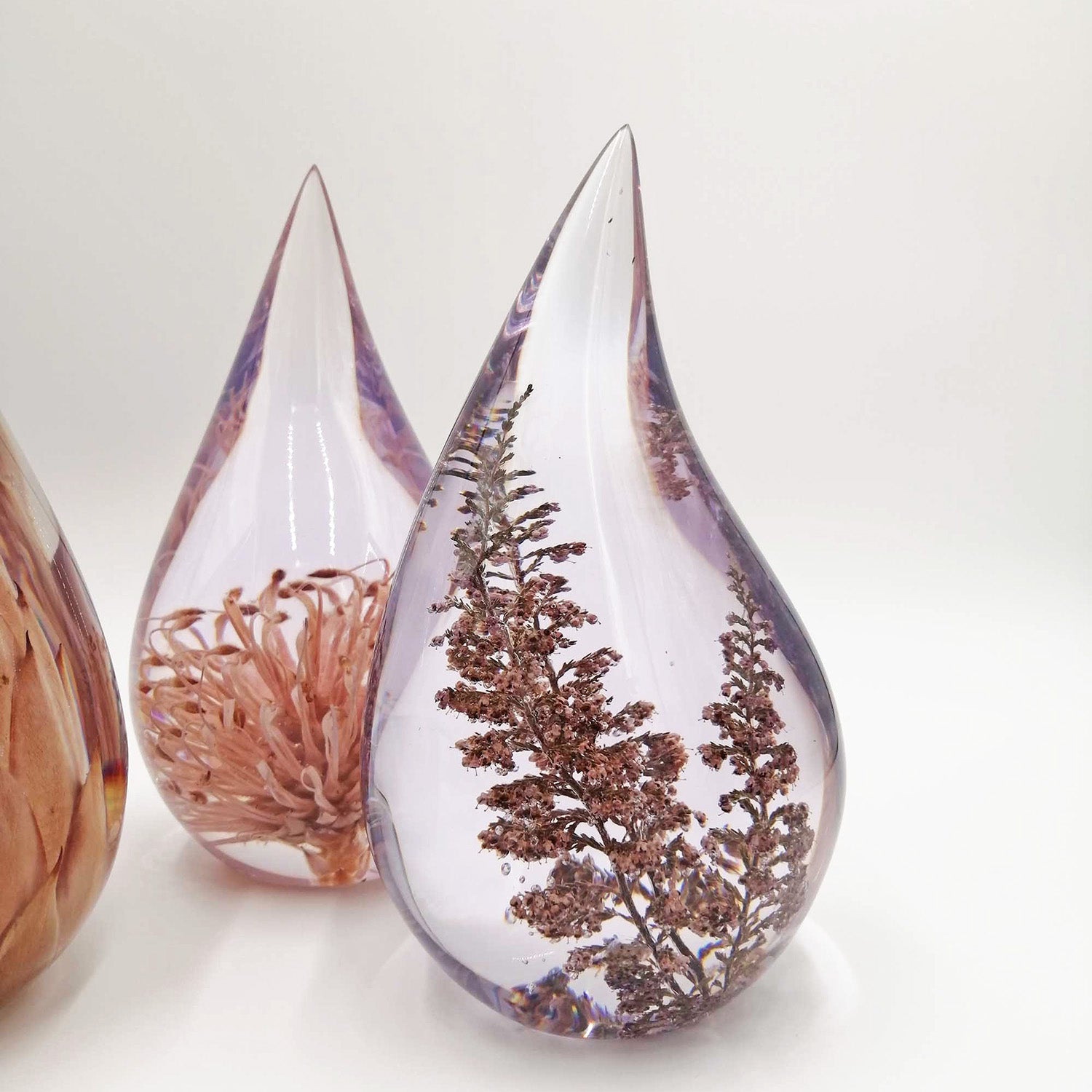 Teardrop-shaped resin containers with preserved flowers on a white background