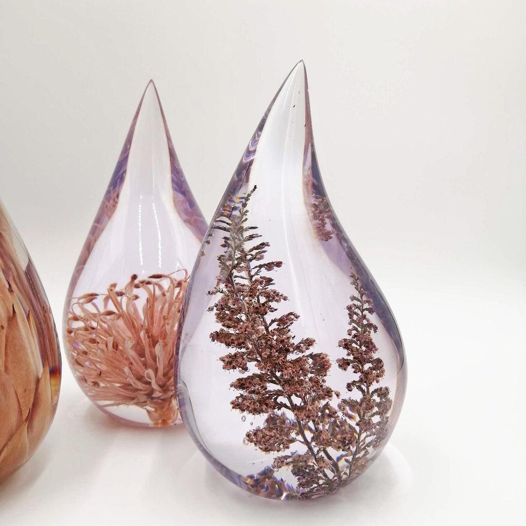 Teardrop-shaped resin containers with preserved flowers on a white background