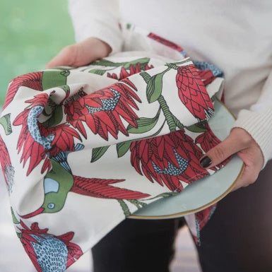 Person holding a fabric-wrapped dish with floral and bird pattern