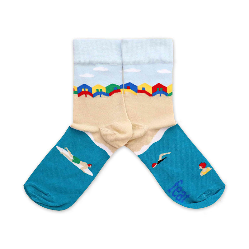 A pair of turquoise socks with a beach hut design, including images of beach scenes and a surfer.