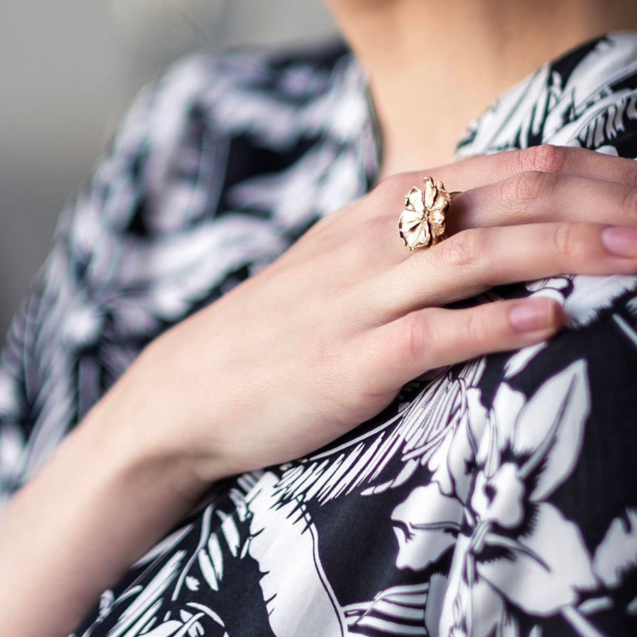 Close-up of a hand wearing a bronze ring with a floral design, against a patterned fabric background.
