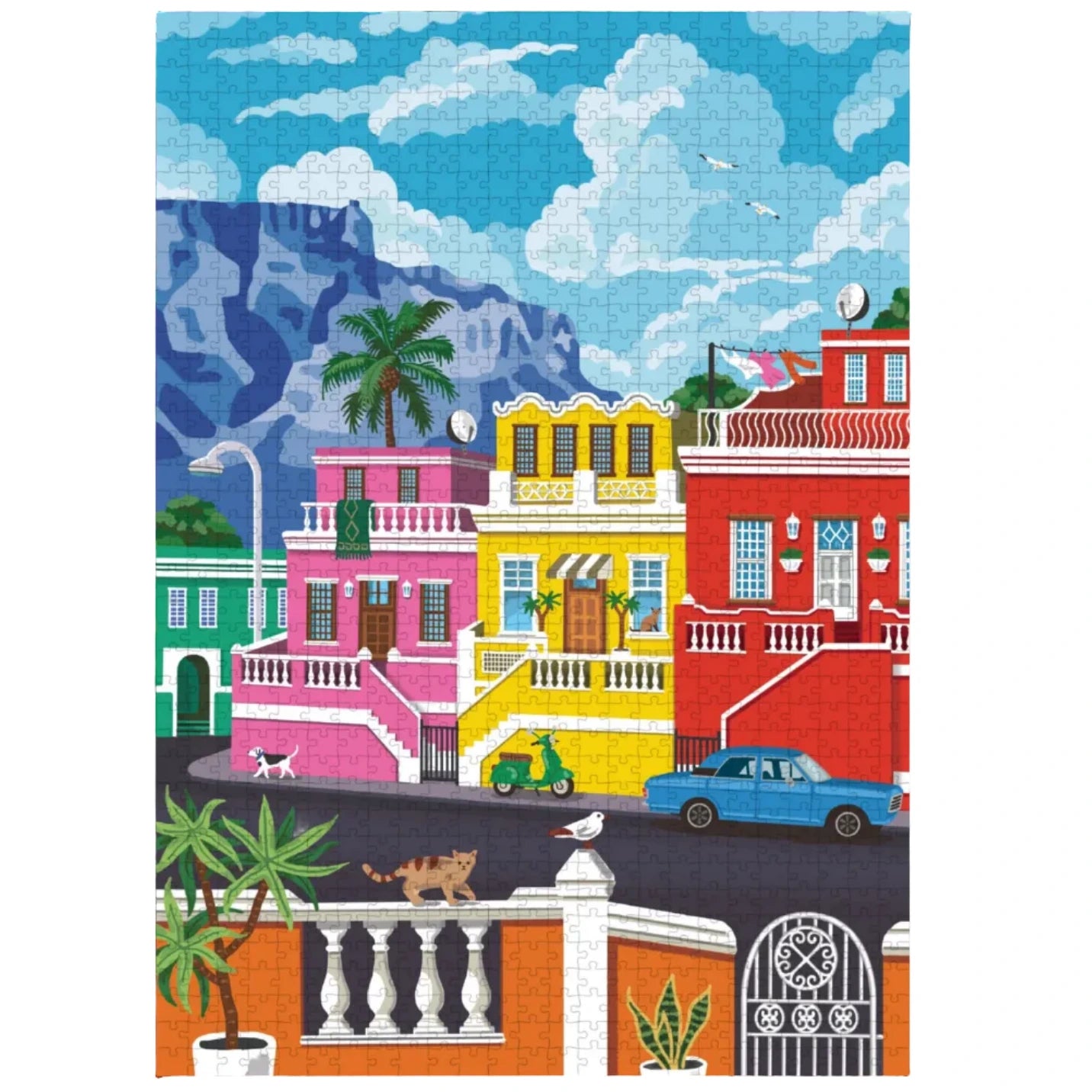 A colorful jigsaw puzzle featuring an illustrated street scene with pink, yellow, and red buildings, a blue car, palm trees, mountains, and a bright blue sky with white clouds.