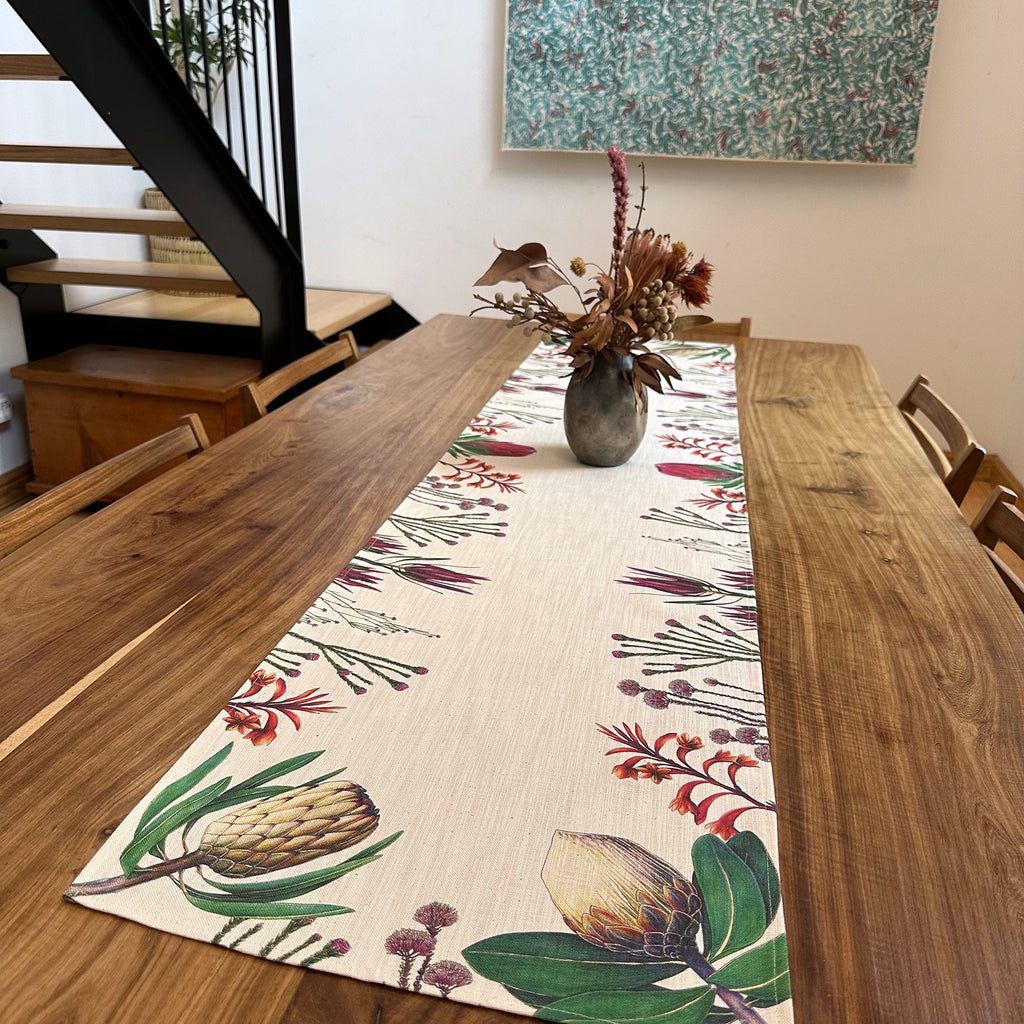Fynbos floral patterned table runner on a wooden dining table with a vase of flowers.