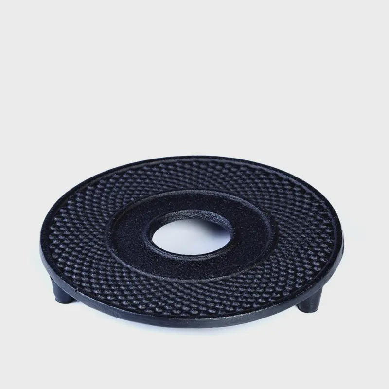A round black cast iron teapot stand with a textured surface, designed to stand under a teapot to protect the table.