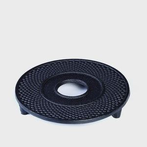 A round black cast iron teapot stand with a textured surface, designed to stand under a teapot to protect the table.
