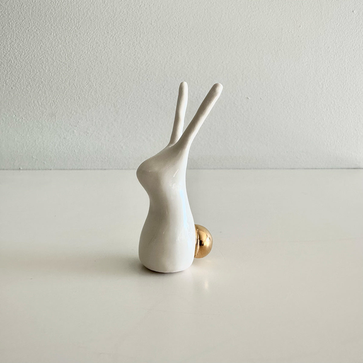 White ceramic rabbit figurine on a light gray surface with a white background
