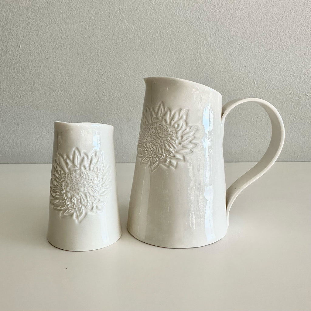 Two white ceramic jugs with embossed floral patterns on a light gray background