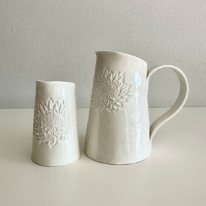 Two white ceramic jugs with embossed floral patterns on a light gray background