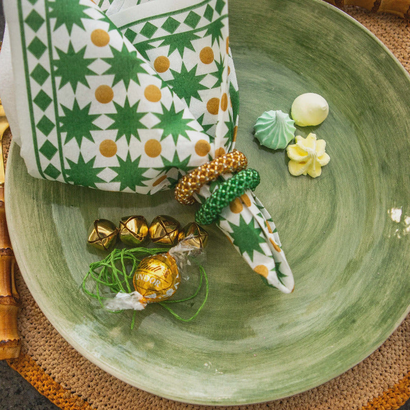 Green plate with decorative items including a green and white patterned bag, gold and green ornaments, and small white flowers.