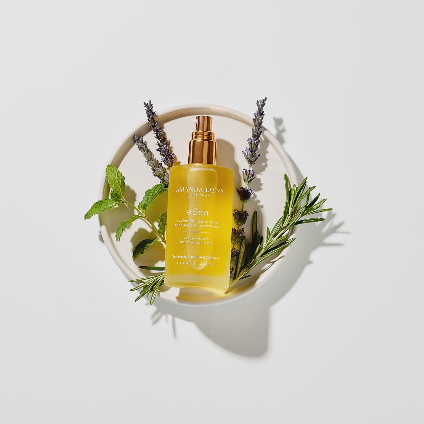 Bottle of Eden Body Oil with herbs on a white background