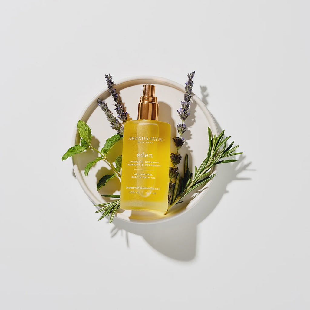 Bottle of Eden Body Oil with herbs on a white background