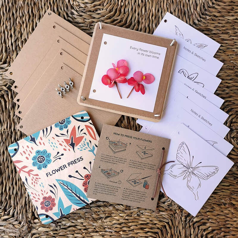 Flower pressing kit with press, cards, and instructions on a woven surface