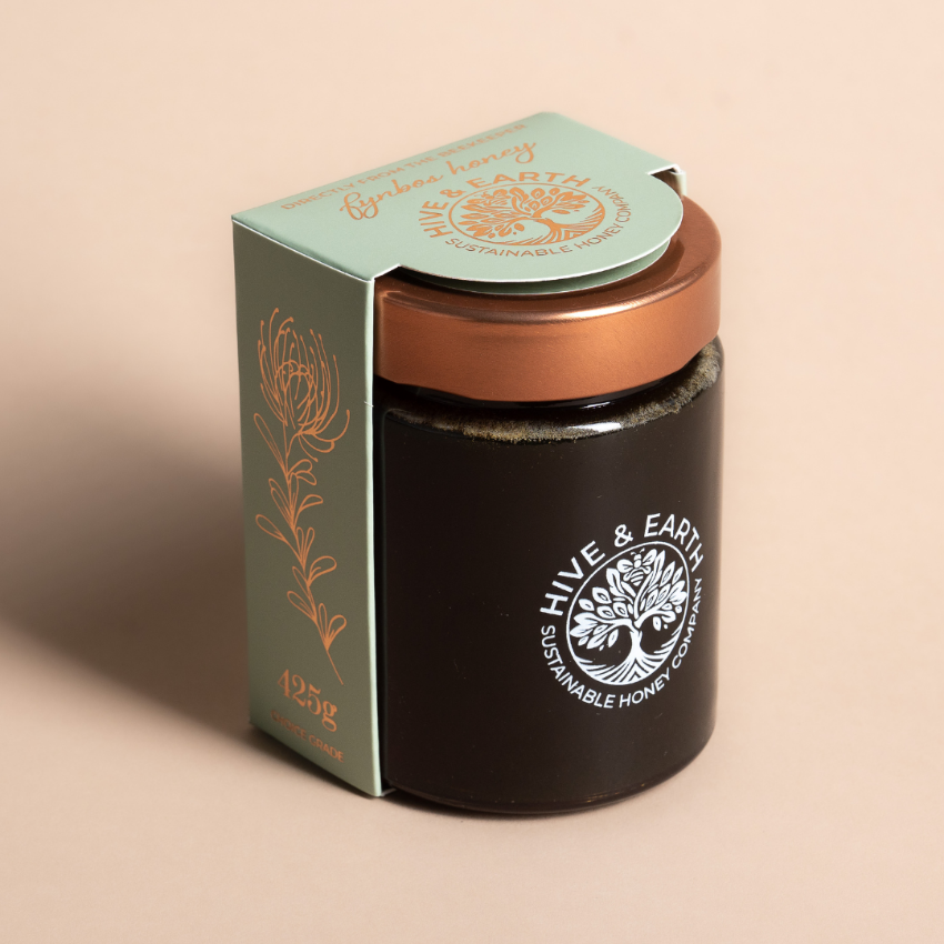 A jar of Hive & Earth Sustainable Honey with its matching green and gold packaging box, set against a solid beige background.