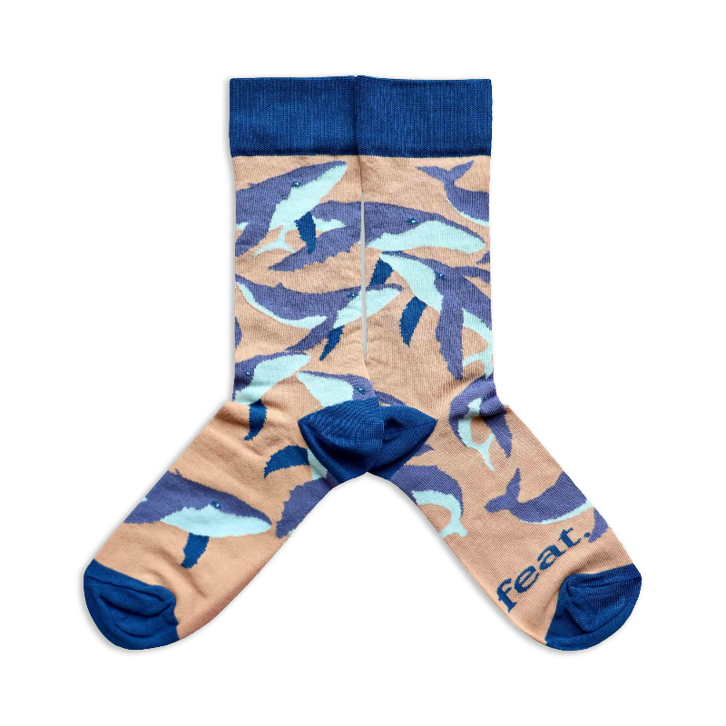 A pair of socks with a beige background featuring humpback whale illustrations.