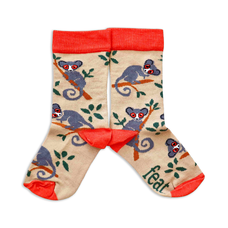 A pair of children's socks with a pattern of bush babies and foliage on a beige background, with red cuffs.