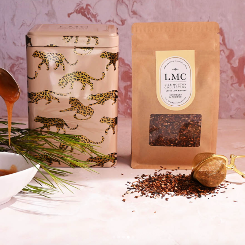 Tea packaging with a decorative tin and a brown paper bag labeled 'LMC' on a light background.