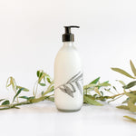 Load image into Gallery viewer, A clear glass bottle with a pump dispenser, labeled &#39;Fynbos body lotion&#39;, placed on a white surface with green foliage in the background.
