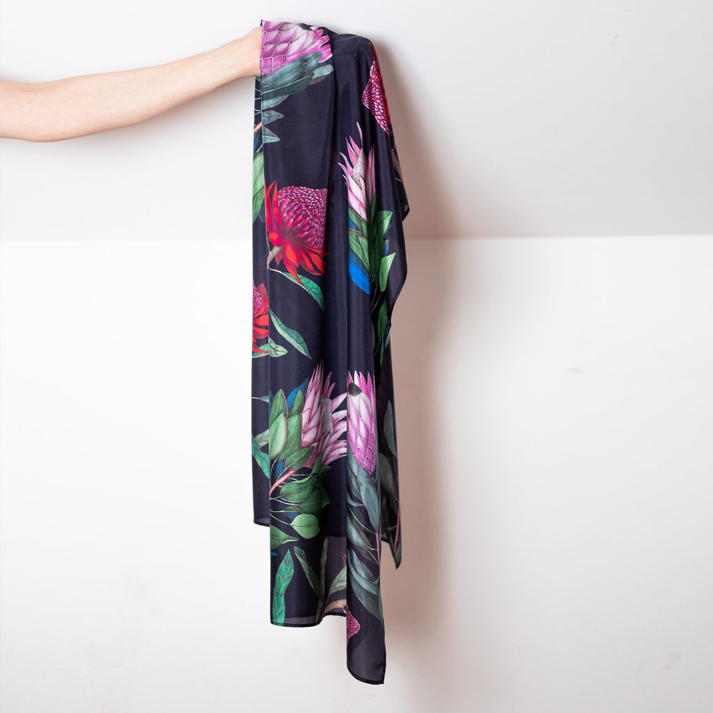 Floral-patterned silk scarf draped over an arm against a white wall