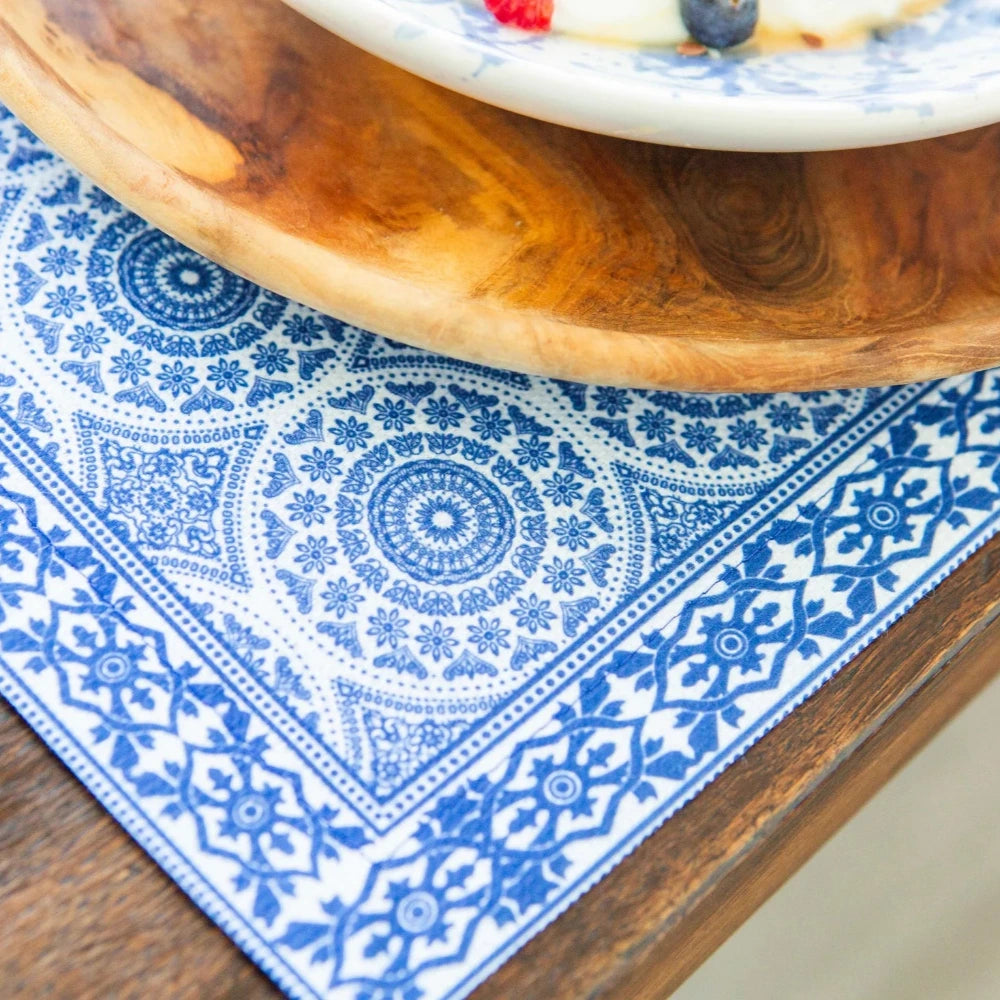 Wooden cutting board on a blue patterned placemat with a blurred plate of fruit in the background.