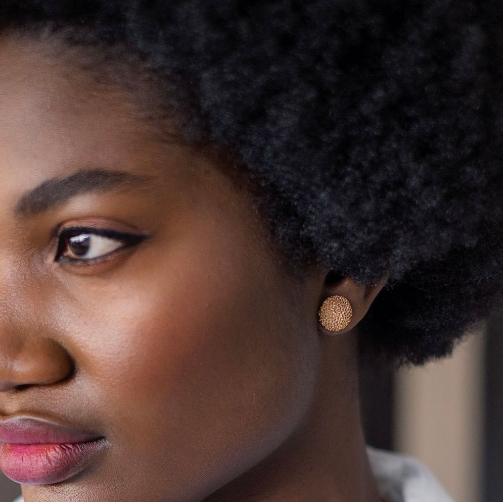Close-up of a woman wearing bronze earrings with a blurred background