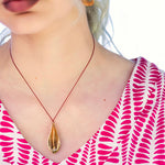 Load image into Gallery viewer, Person wearing a bronze pendant necklace with a red cord, against a blurred background.
