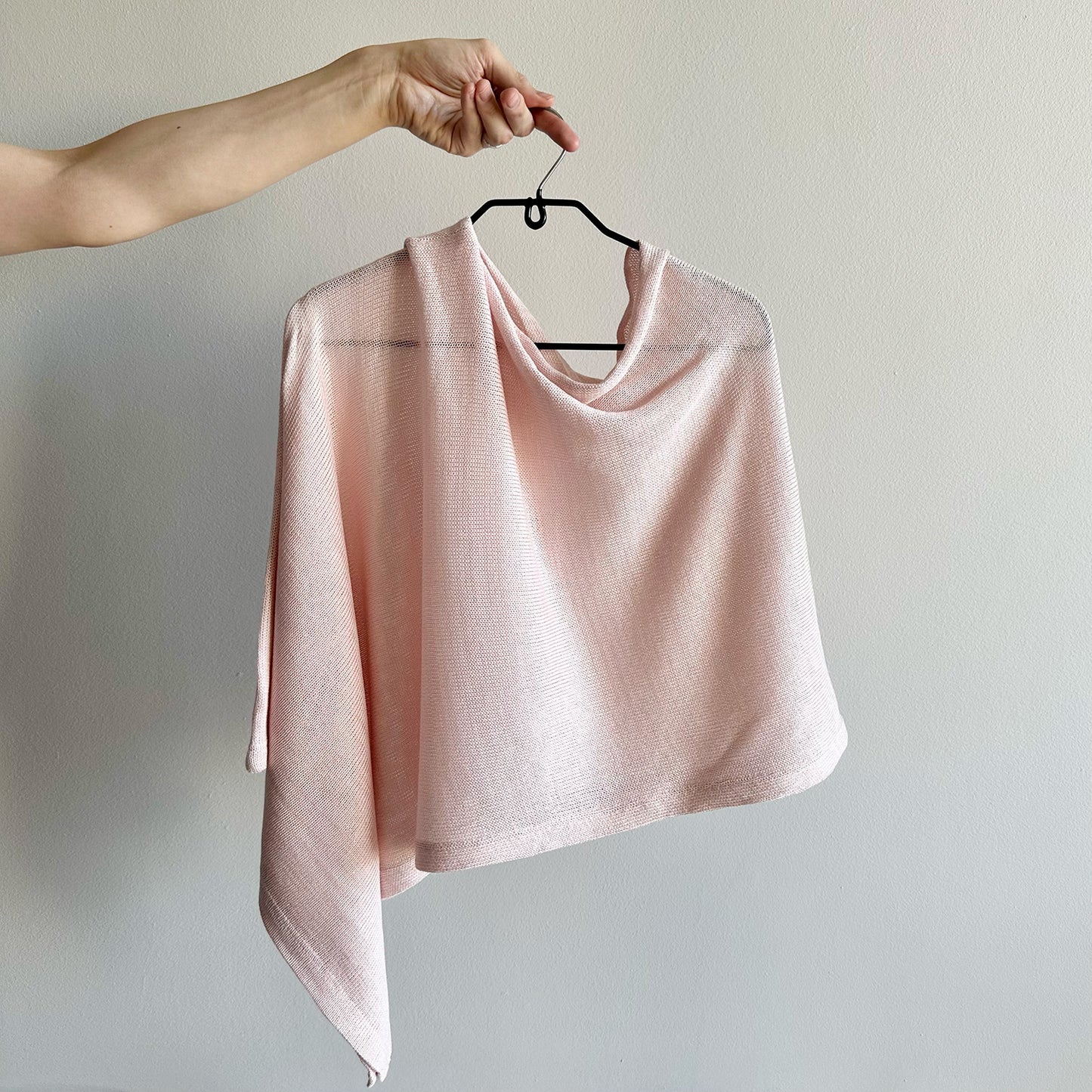 Pink poncho on a hanger against a plain background
