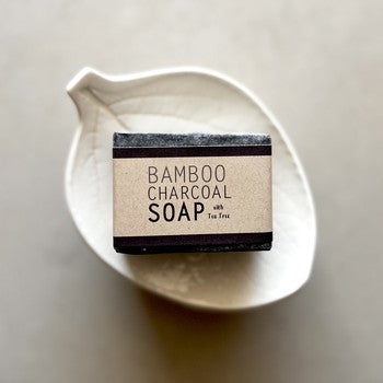 Bar of bamboo charcoal soap in a white dish on a neutral background