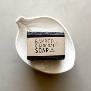 Bar of bamboo charcoal soap in a white dish on a neutral background