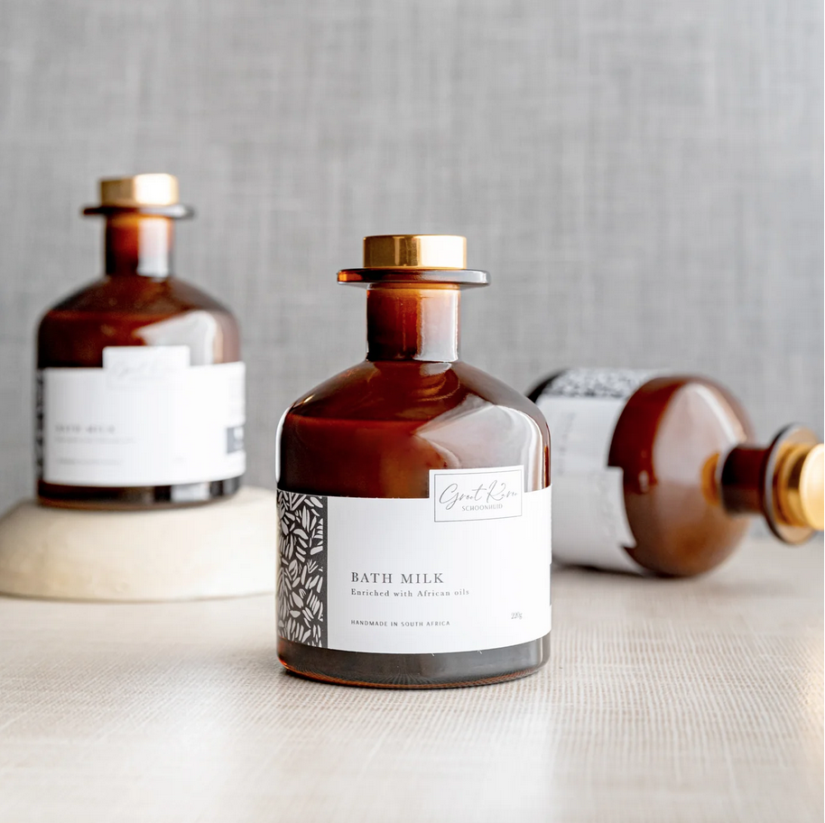 Bottle of bath milk with a gold cap on a light surface