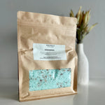 Load image into Gallery viewer, Brown paper bag with a label and visible blue bath salts on a gray background
