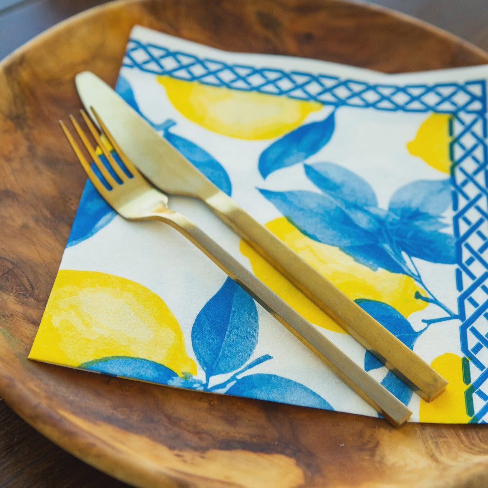 Gold fork and knife on a colorful napkin with lemon and leaf pattern on a wooden plate.