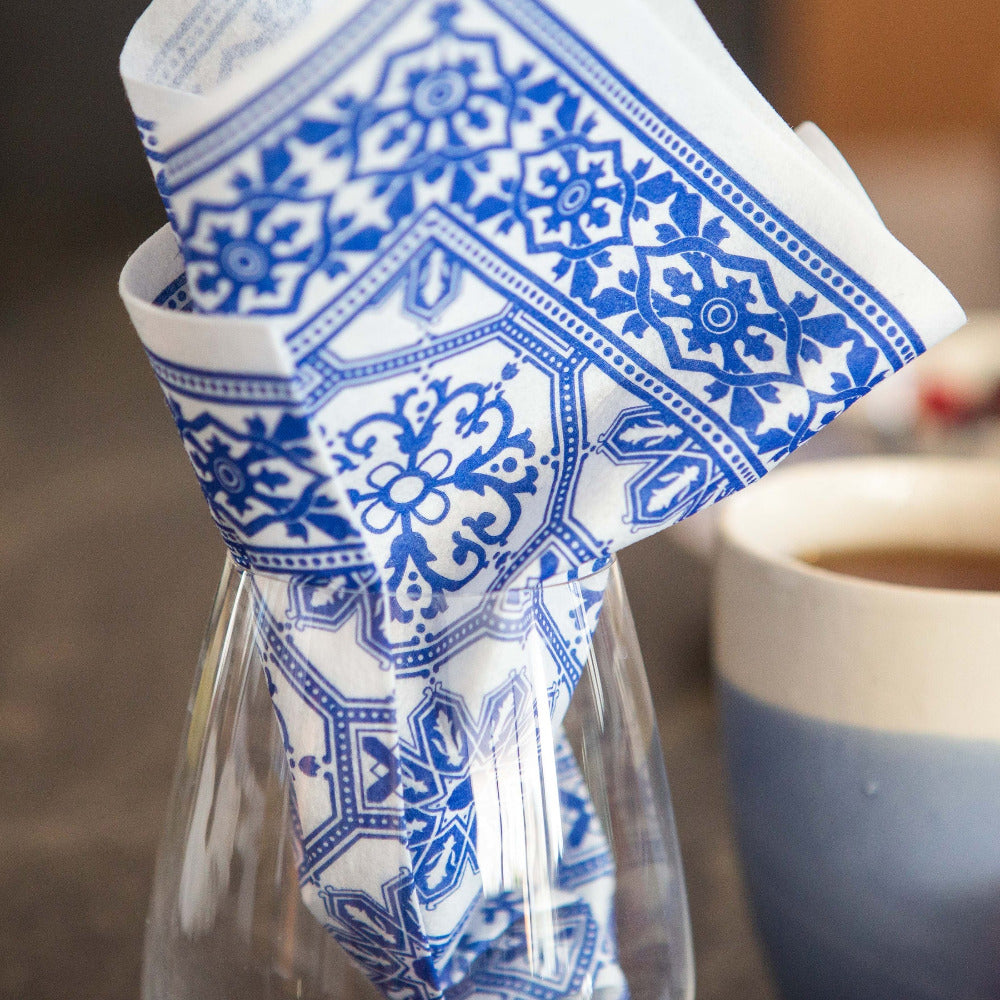 Blue and white patterned napkin in a glass with a blurred cup in the background
