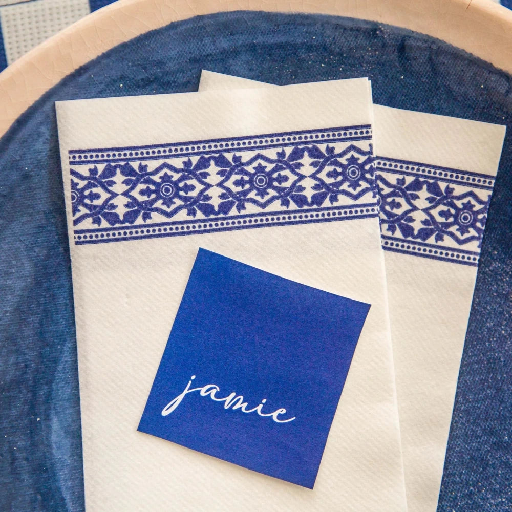 White towel with blue pattern and namecard on a blue textured dish.