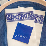 Load image into Gallery viewer, White towel with blue pattern and namecard on a blue textured dish.

