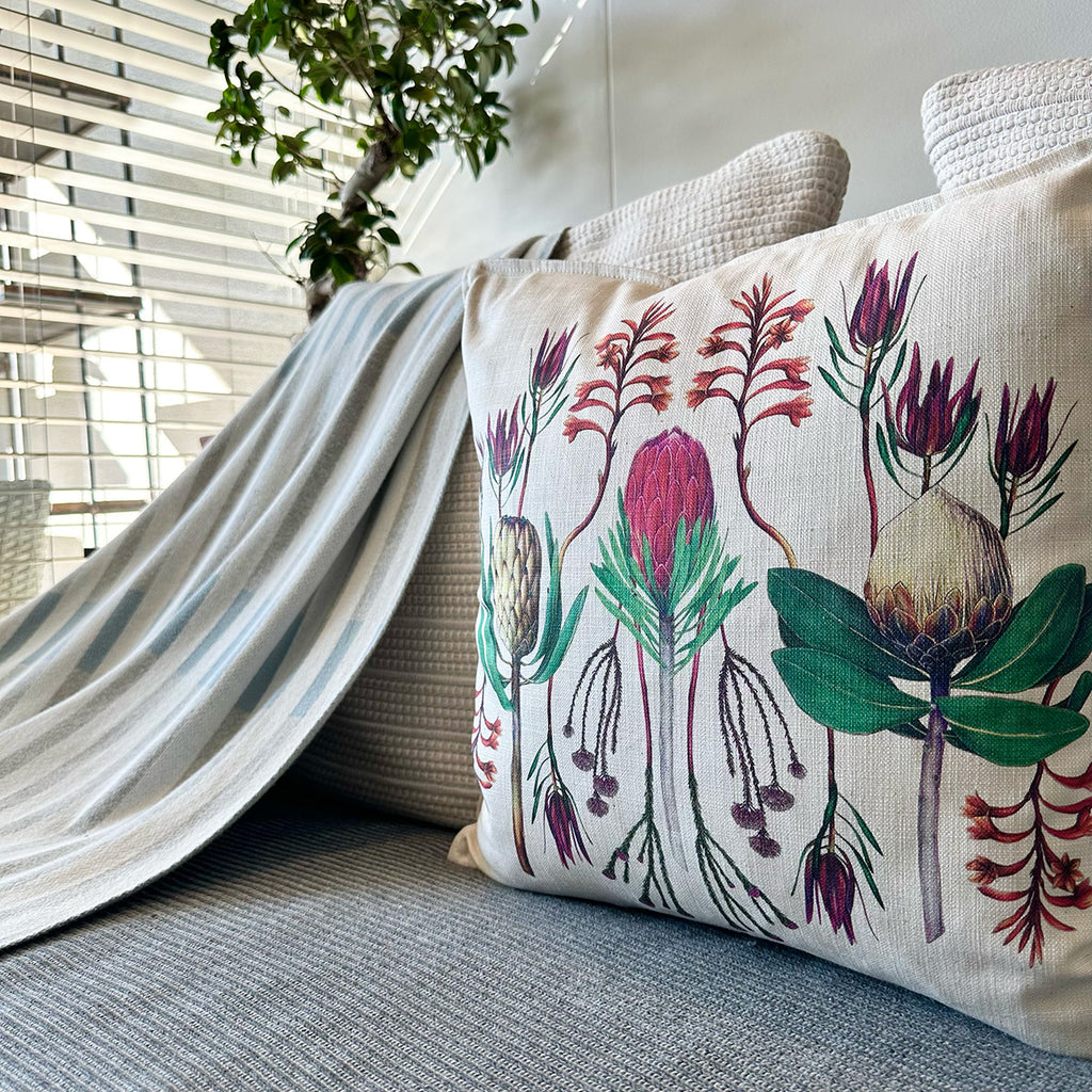 Decorative pillow with fynbos floral design on a couch next to a plant