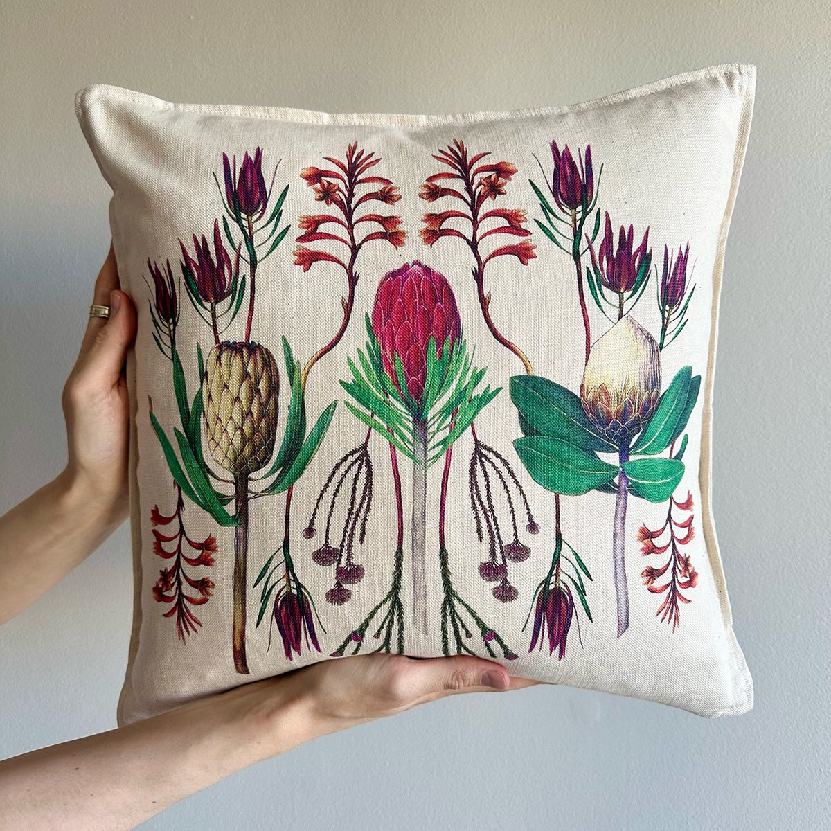 Decorative pillow with fynbos floral design held by a hand against a plain background