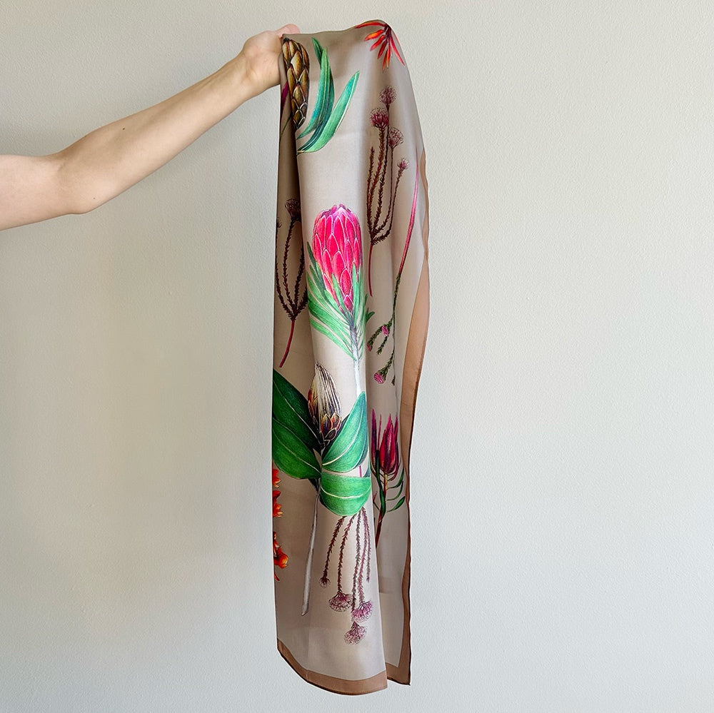 Silk scarf with floral design held by a hand against a plain background