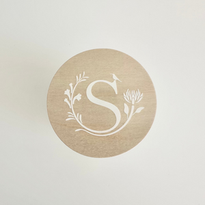 Round wooden lid with a white monogram 'S' design on a light gray background