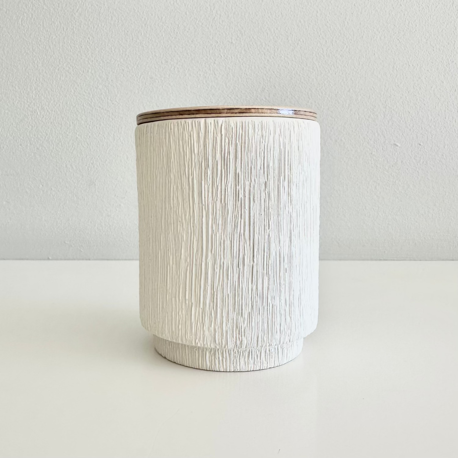 White textured candle jar with wooden lid on a light gray background