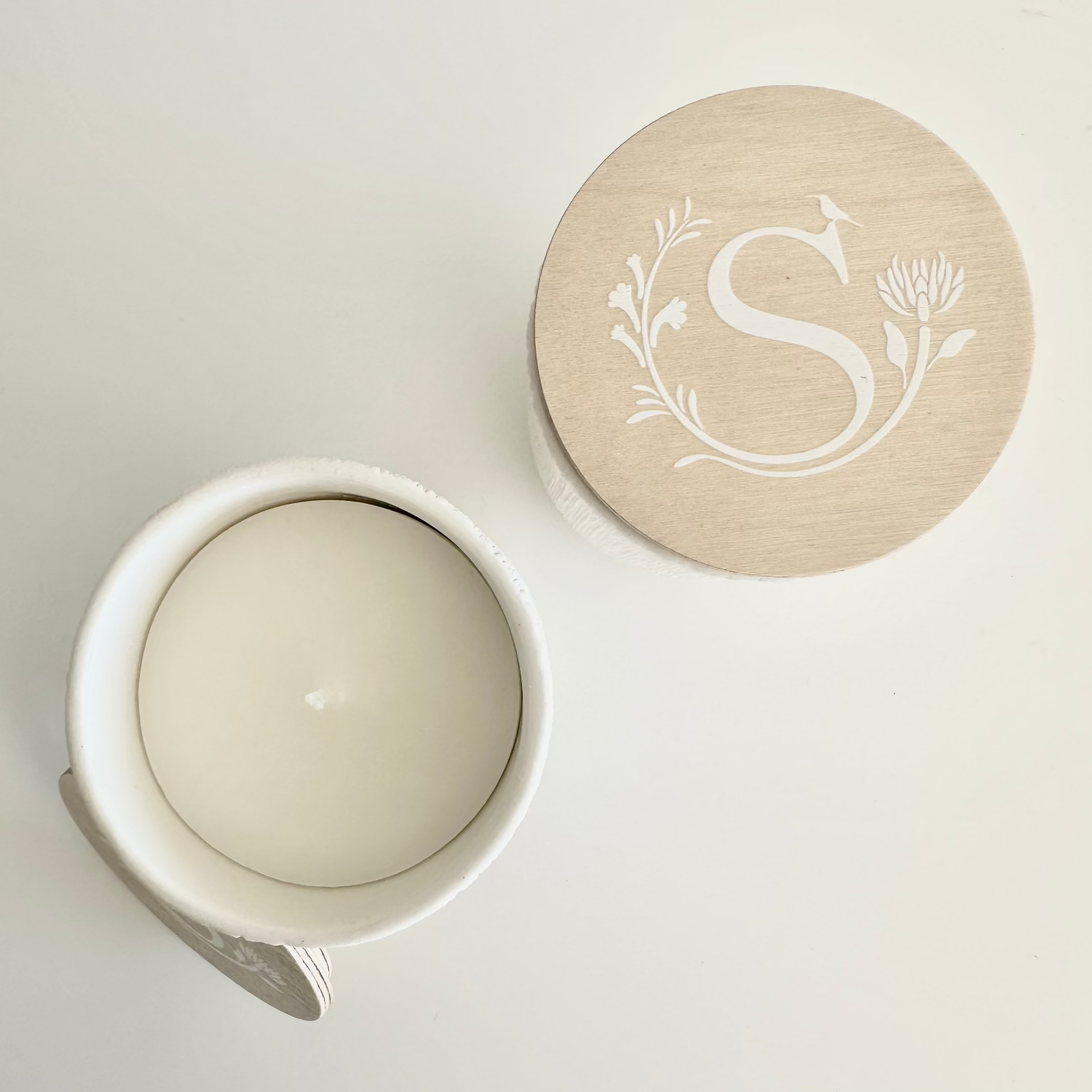 White ceramic jar with a beige lid featuring a monogram on a light gray background