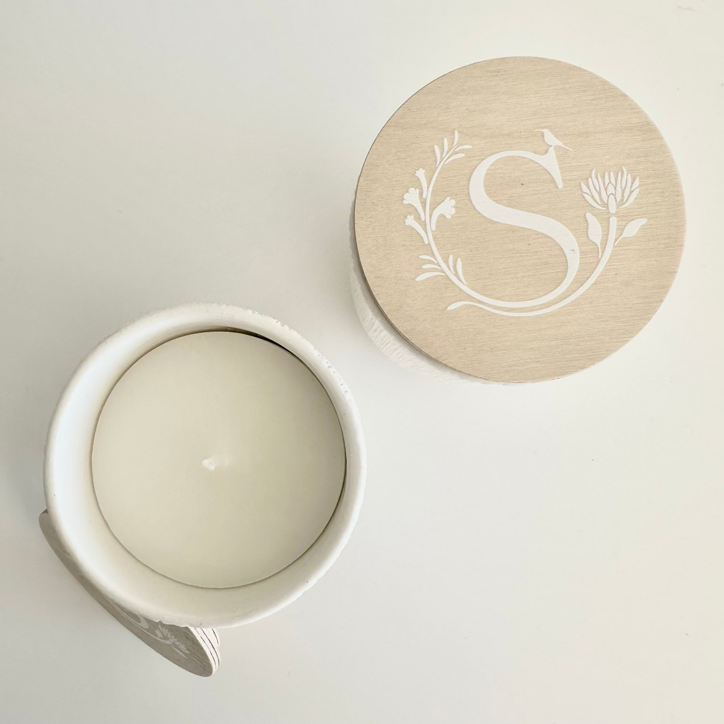 White ceramic jar with a beige lid featuring a monogram on a light gray background