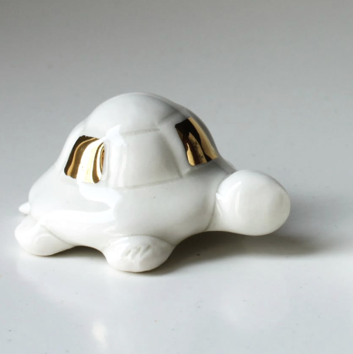 White ceramic turtle figurine with gold accents on a gray background