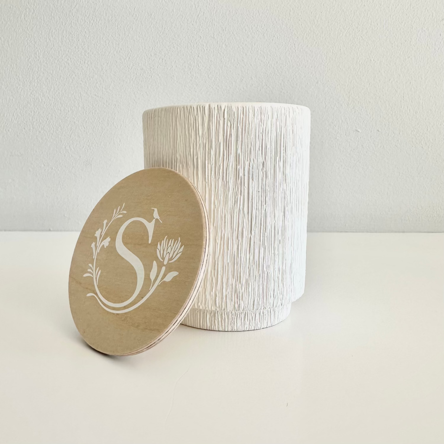 White textured container with a wooden lid featuring a monogram on a light background