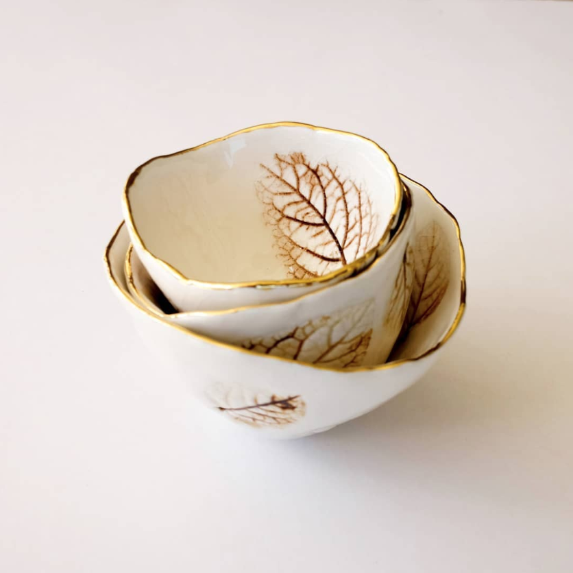 Three ceramic bowls with gold leaf patterns on a white background