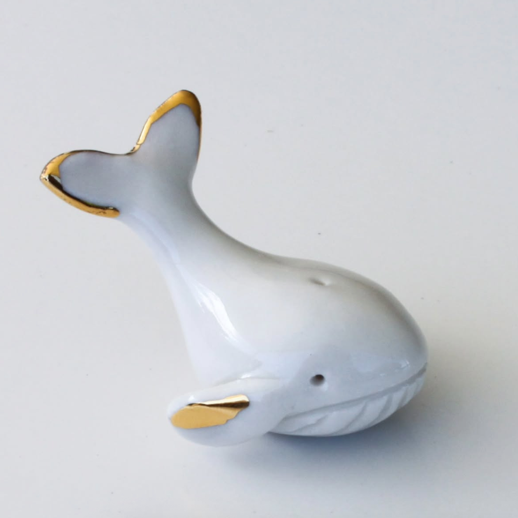 White ceramic whale figurine with gold accents on a light gray background
