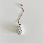Load image into Gallery viewer, White ceramic pine cone ornament on a string against a light gray background
