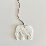 Load image into Gallery viewer, White elephant-shaped decoration on a string against a light gray background
