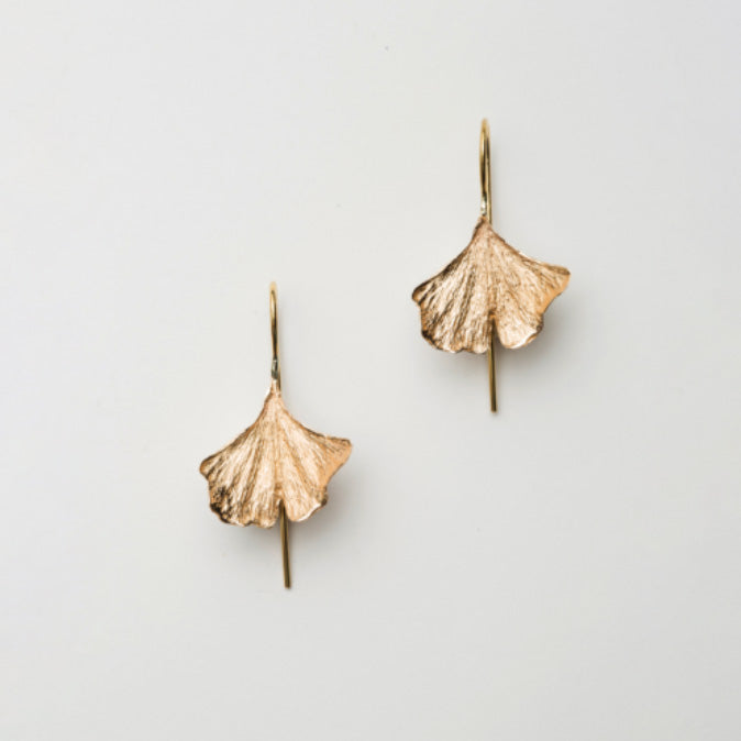 Pair of bronze leaf-shaped earrings on a light gray background